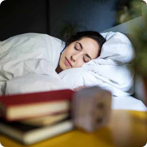 a woman sleeping in bed with books on a table