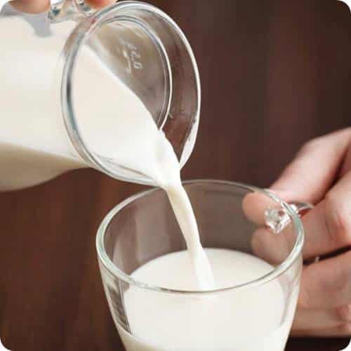 a person pouring milk into a glass